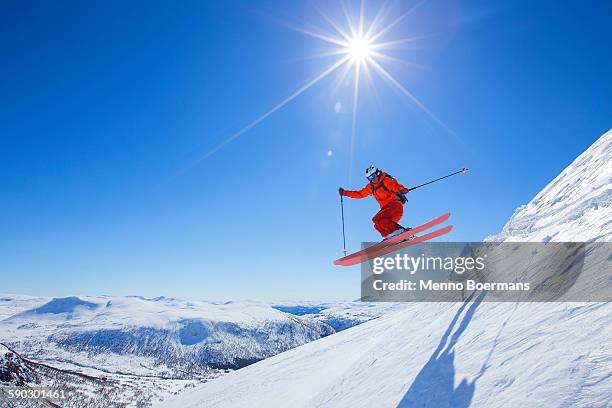 a male freerider in a red suit is jumping from a snow ridge. the sun is shining, the sky is blue.   - ski foto e immagini stock