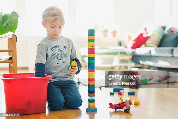 girl playing with toy blocks while kneeling on floor at home - toy box fotografías e imágenes de stock