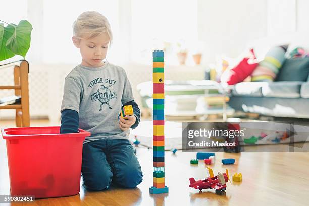 girl playing with toy blocks while kneeling on floor at home - toy box stock pictures, royalty-free photos & images