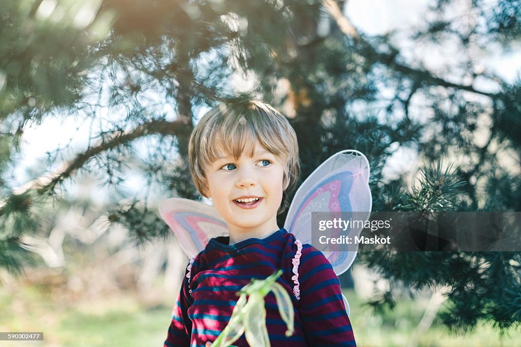 Happy boy in fairy wings looking away at yard