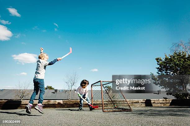 excited girl playing hockey with boy at yard against blue sky - blue sky friends photos et images de collection