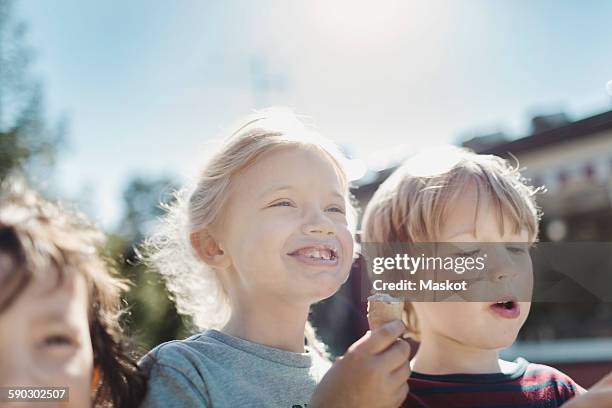 low angle view of friends eating ice creams at yard on sunny day - boy and girl eating ice cream stock-fotos und bilder