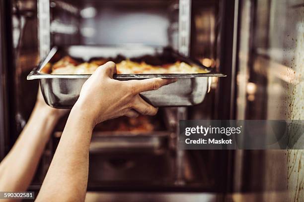 cropped image of female chef putting dish in oven - chef kitchen stockfoto's en -beelden