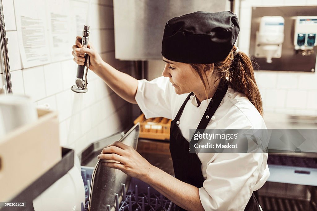 Female chef spraying water on plates in commercial kitchen