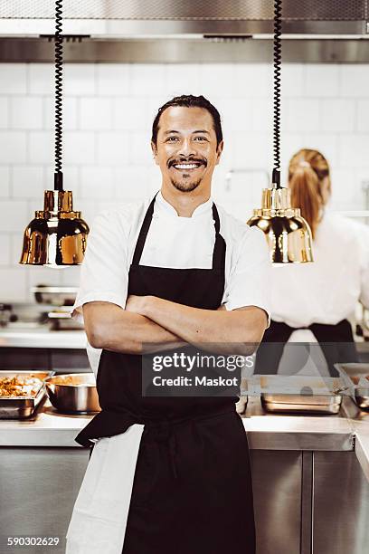 portrait of happy male chef standing arms crossed in commercial kitchen - tablier photos et images de collection