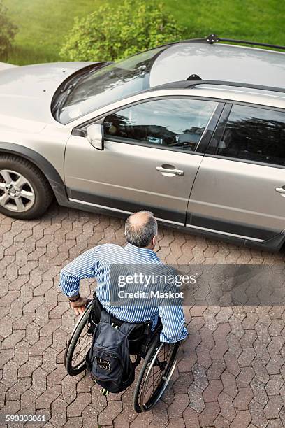 high angle view of mature man in wheelchair moving towards car on street - car exterior rear high angle stock-fotos und bilder