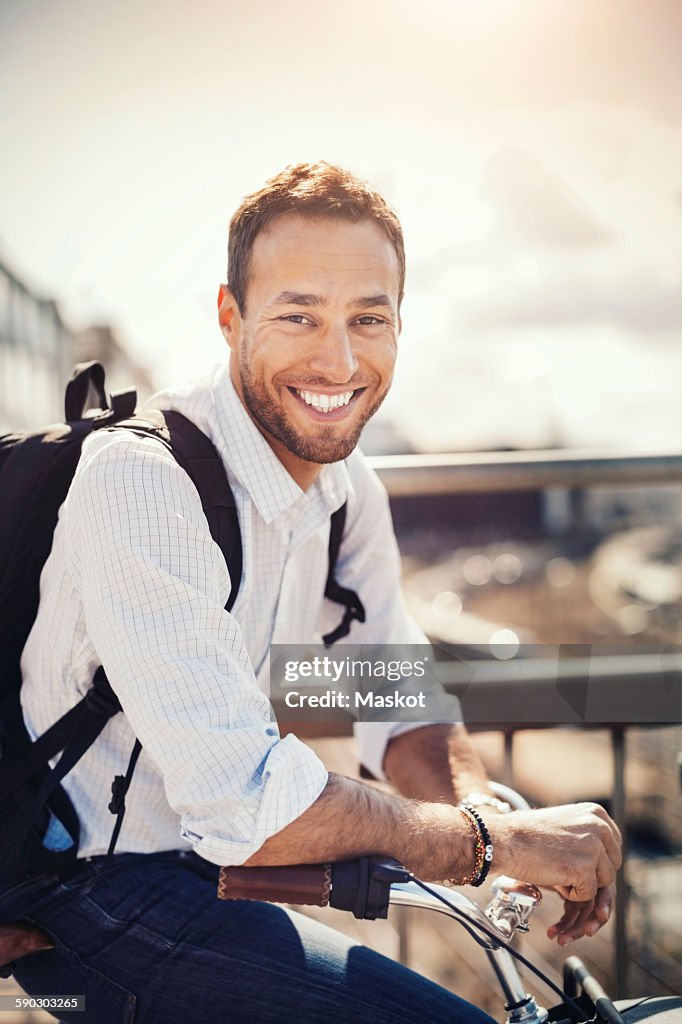 Portrait of happy businessman leaning on bicycle against sky