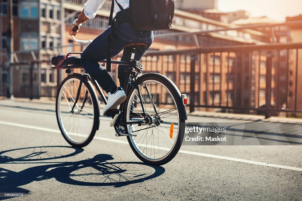 Low section of businessman riding bicycle on bridge in city