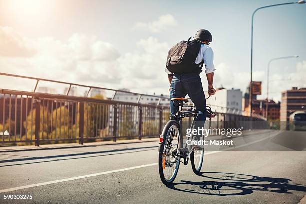rear view of businessman riding bicycle on bridge in city - radfahren stock-fotos und bilder