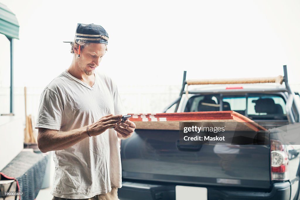 Carpenter using mobile phone by pick-up truck against clear sky