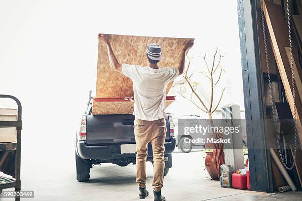 rear view of man loading wooden planks in pick-up truck - pick up stock pictures, royalty-free photos & images