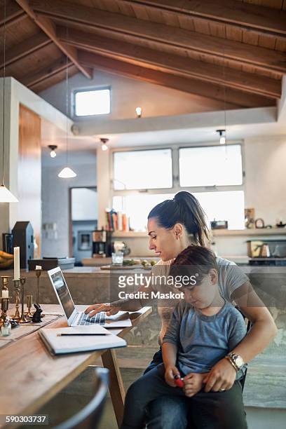 son sitting with mother working on laptop at dining table - auf dem schoß stock-fotos und bilder