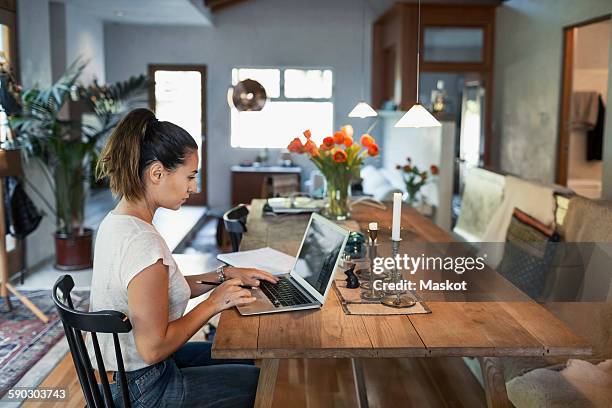 side view of woman working on laptop at dining table - dining table icon stock pictures, royalty-free photos & images