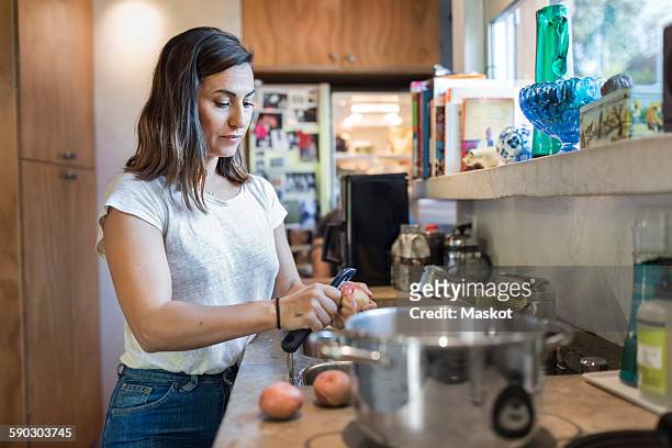 woman peeling potato at kitchen counter - geschält stock-fotos und bilder