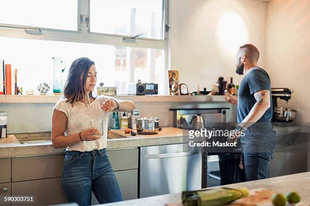 woman checking time while man looking through window in kitchen - checking watch stock pictures, royalty-free photos & images