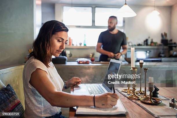 side view of woman working at dining table while man standing in background - woman table standing stock pictures, royalty-free photos & images
