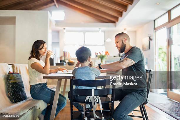 family of three sitting at dining table in house - esstisch stock-fotos und bilder