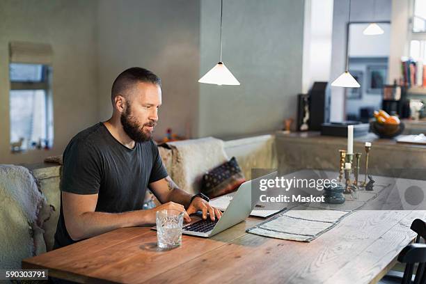man working on laptop at dining table in house - matbord bildbanksfoton och bilder