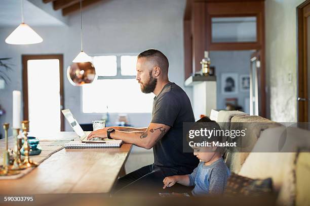 side view of father and son using technologies at dining table - parent on computer stockfoto's en -beelden