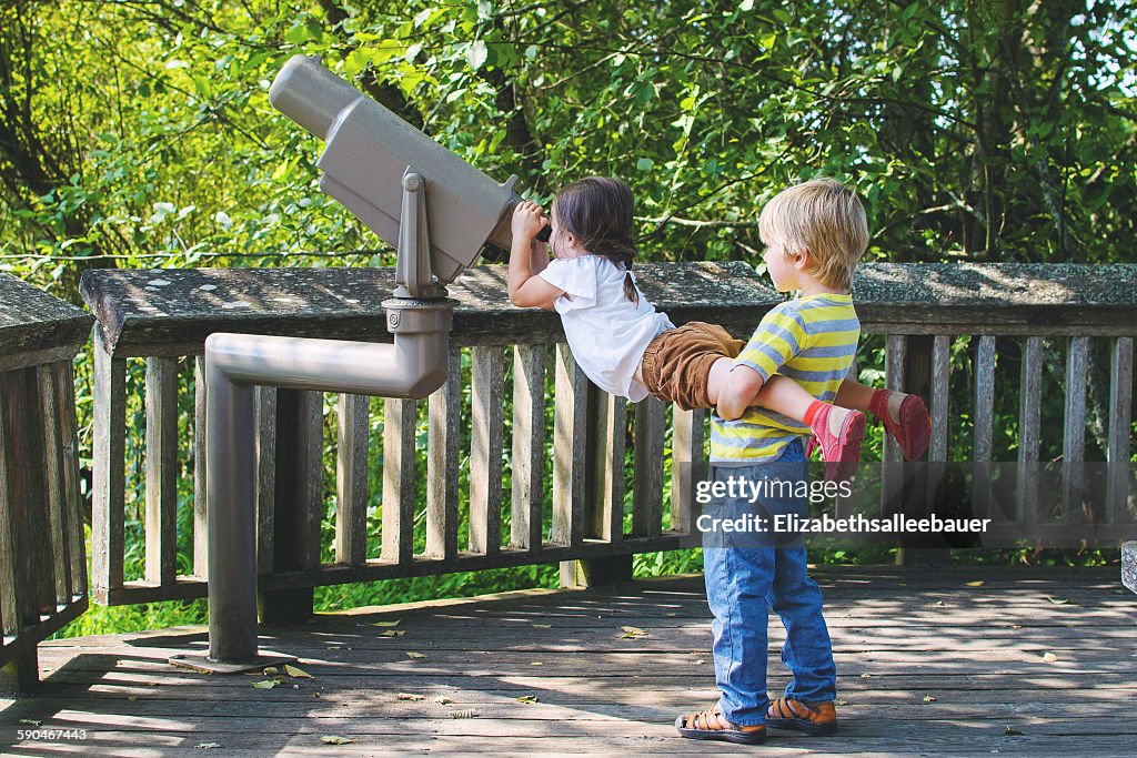 Boy lifting girl to look through telescope