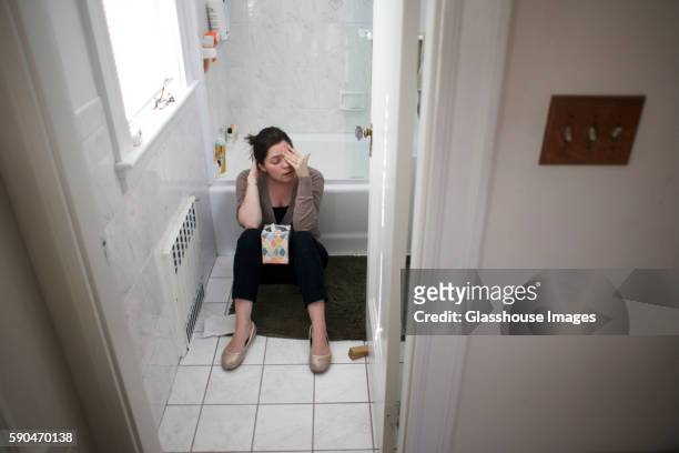 pregnant woman sitting on bathroom floor with box of tissues between knees - brechreiz stock-fotos und bilder