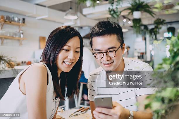 couple looking at smartphone with smile in cafe - yiu yu hoi stock pictures, royalty-free photos & images