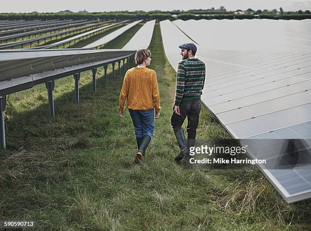 male and female farmers walking through solar farm - couple farm photos et images de collection