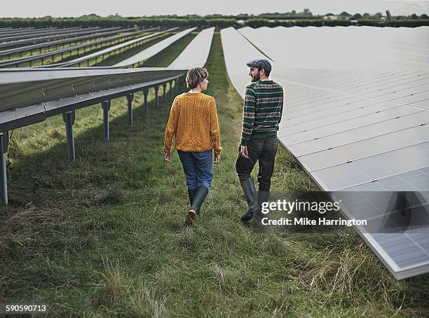 male and female farmers walking through solar farm - farmer walking stock pictures, royalty-free photos & images