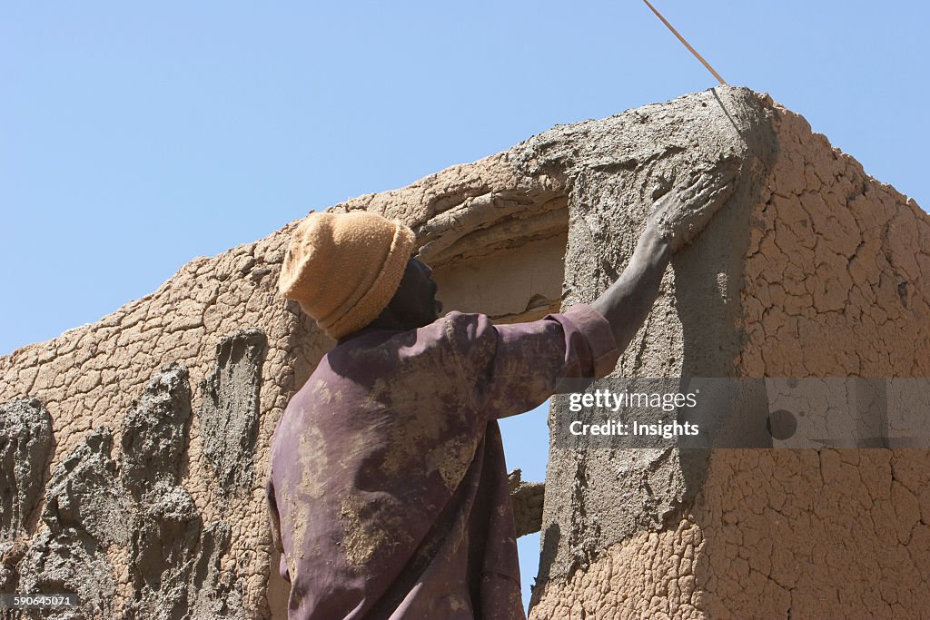 Man applying mud to a house.