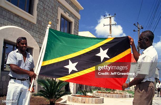 West Indies, Nevis, Two Men Holding St Kitts And Nevis Flag By Government Building.