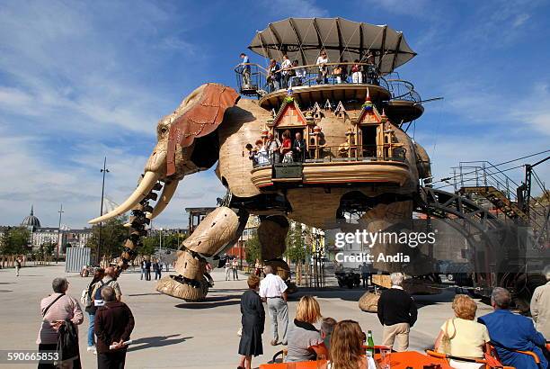 Nantes , Giant elephant of the "Machines de l'ile" with passengers on board for a walk on the former shipyards' site. People seated behind tables at...