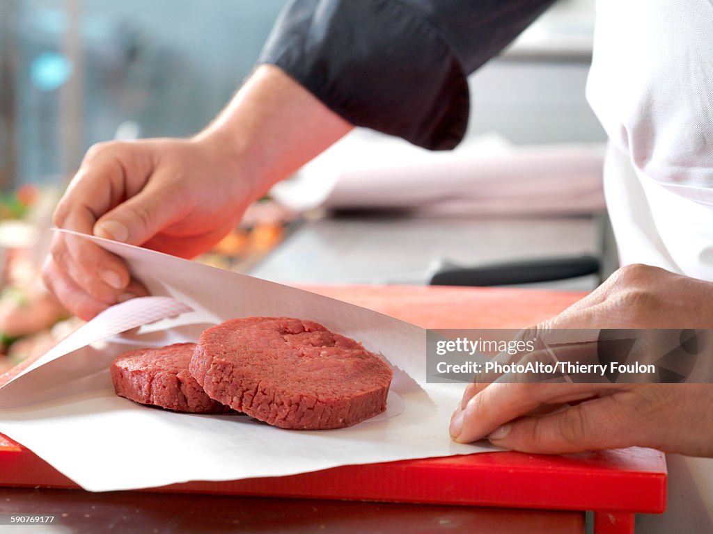 Butcher wrapping beef patties in wax paper, cropped