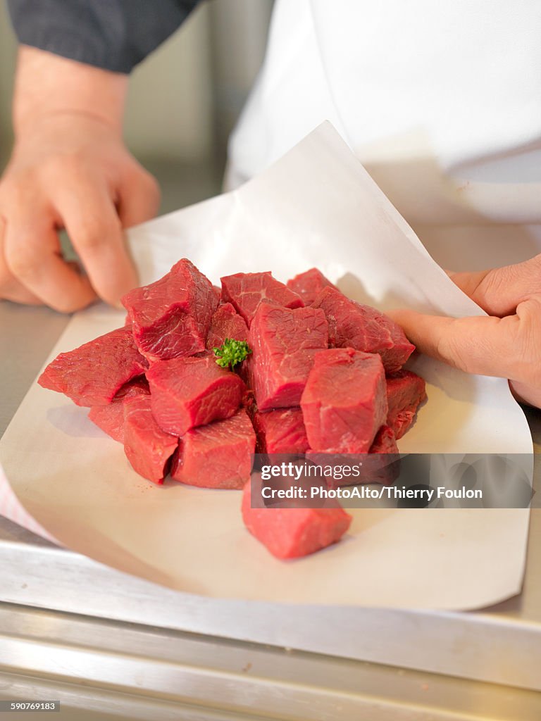 Butcher wrapping meat cubes in wax paper, cropped