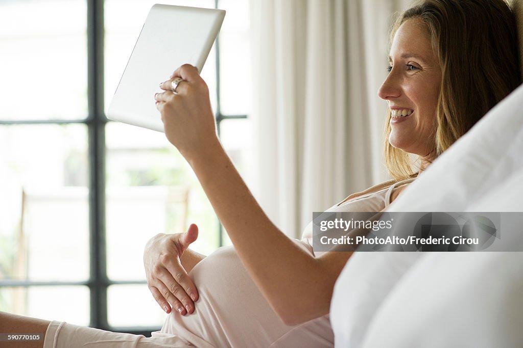Pregnant woman using digital tablet to video chat with friends and family
