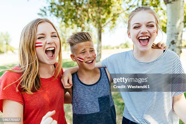 austria, three teenagers with national colors painted on their cheeks celebrating together - faces of a nation stock-fotos und bilder
