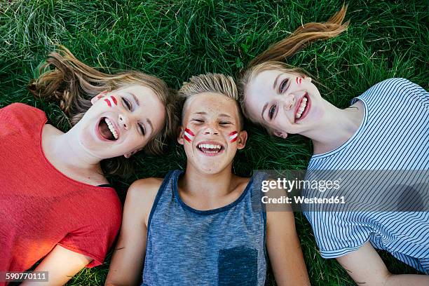 austria, three teenagers with national colors painted on their cheeks lying on a meadow - faces of a nation stock-fotos und bilder