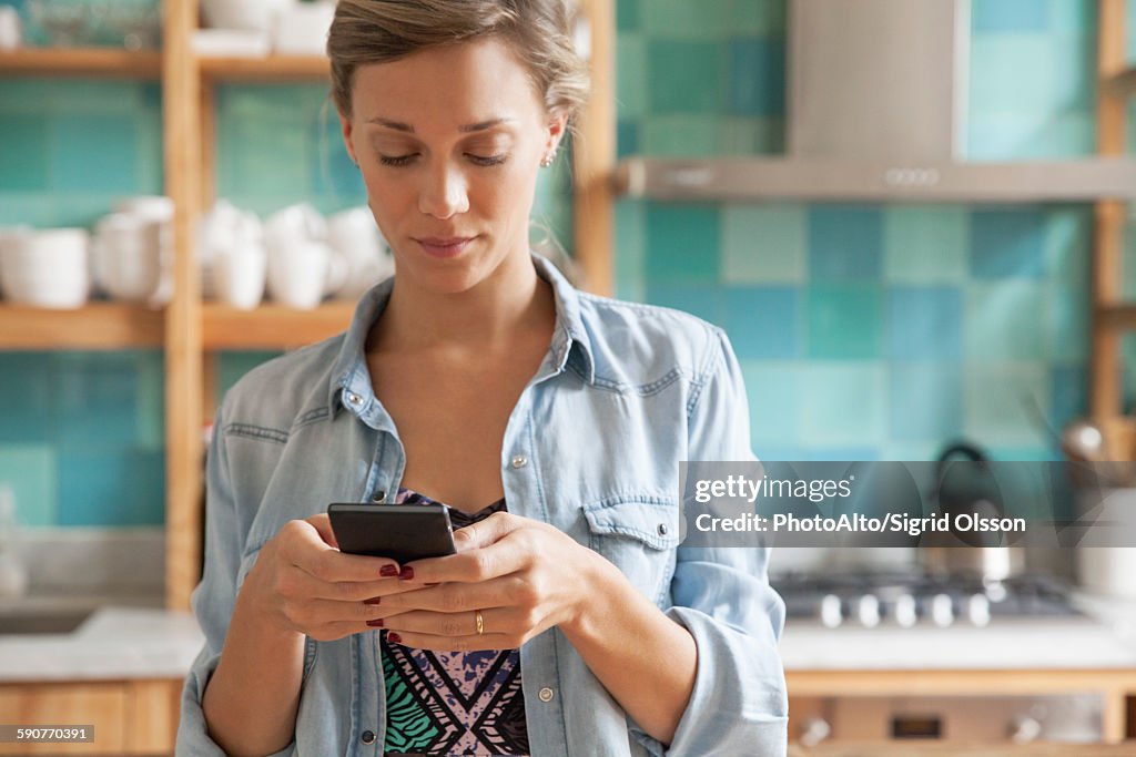 Young woman standing in kitchen with cell phone