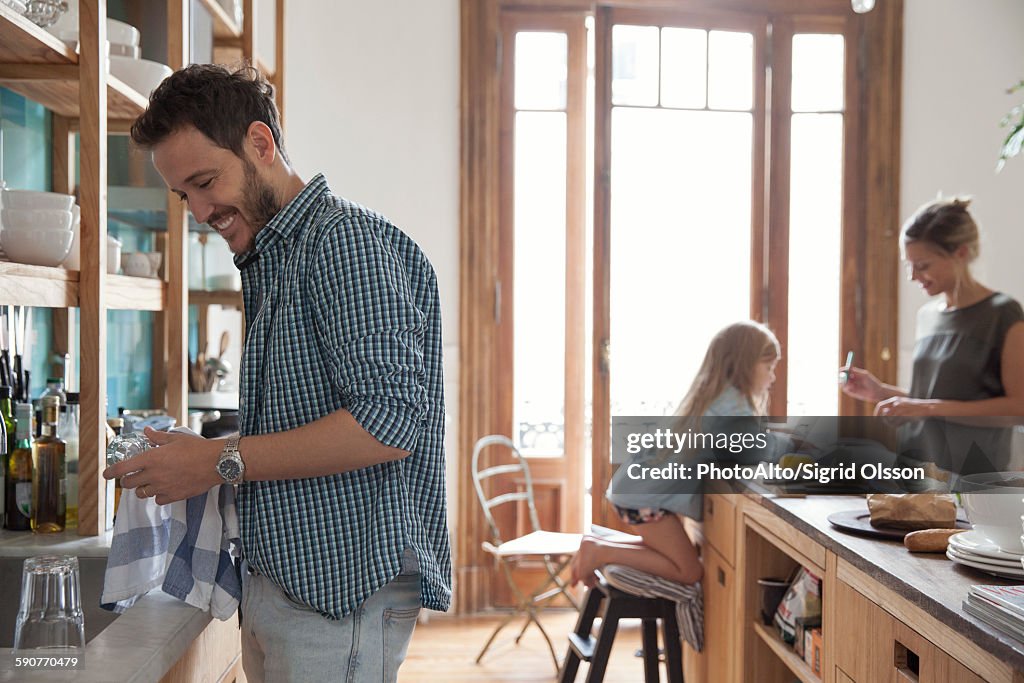 Family in kitchen, man drying dishes in foreground