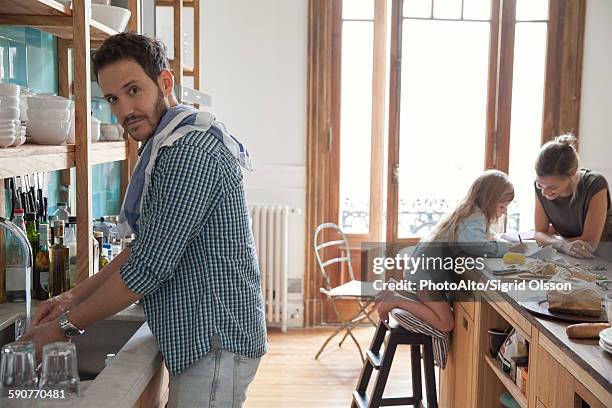 family in kitchen, man doing dishes in foreground - faire la vaisselle photos et images de collection