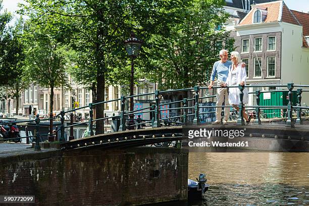 netherlands, amsterdam, senior couple walking on a bridge - amsterdam canal stockfoto's en -beelden