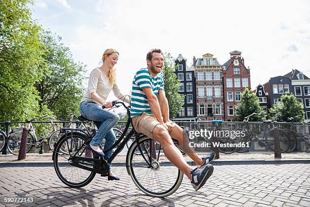 netherlands, amsterdam, happy couple riding bicycle in the city - amsterdam bike stock-fotos und bilder