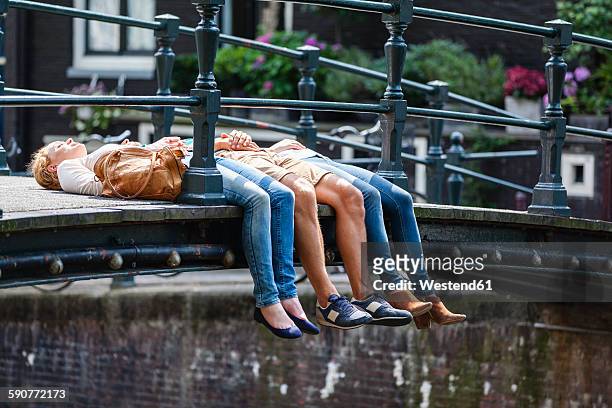 netherlands, amsterdam, three friends lying on bridge - amsterdam bridge stock pictures, royalty-free photos & images