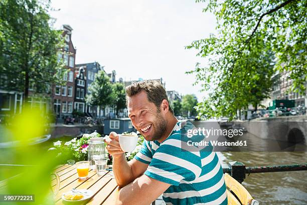 netherlands, amsterdam, happy man drinking cup of coffee at town canal - sidewalk cafe stock pictures, royalty-free photos & images