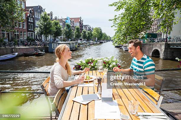 netherlands, amsterdam, happy couple having lunch at town canal - kanal stock-fotos und bilder