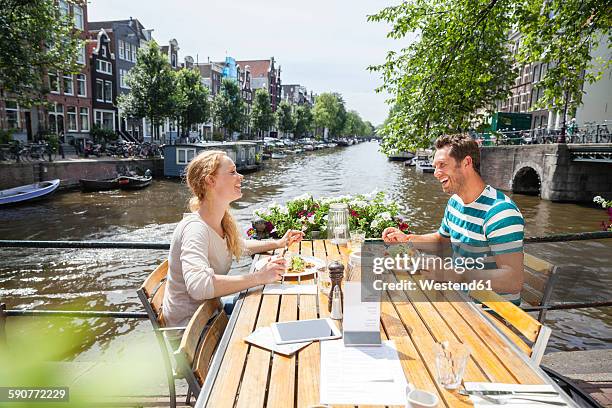 netherlands, amsterdam, happy couple having lunch at town canal - amsterdam canal stockfoto's en -beelden