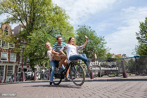 netherlands, amsterdam, three playful friends riding on one bicycle in the city - amsterdam bike stockfoto's en -beelden