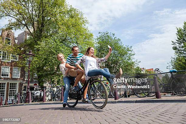 netherlands, amsterdam, three playful friends riding on one bicycle in the city - amsterdam people stock pictures, royalty-free photos & images