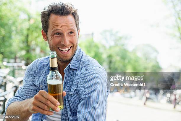 netherlands, amsterdam, happy man drinking beer from bottle - beer bottles stockfoto's en -beelden