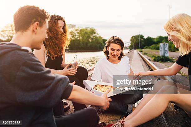 friends sitting together outdoors sharing a pizza - sharing pizza stock pictures, royalty-free photos & images