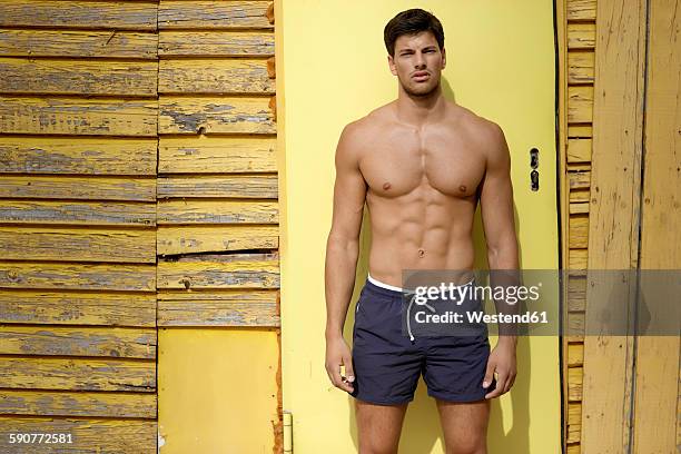 portrait of athletic young man standing in front of yellow wooden wall - abs stock pictures, royalty-free photos & images